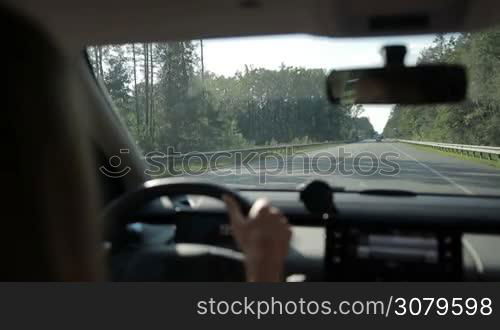 Woman driving car on motorway through the forest in sunlight. View from vehicle&acute;s interior. Car travelling on asphalt highway over beautiful landscape background.