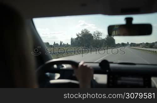 Woman driving car on motorway with rural scene on background. View from inside of vehicle&acute;s interior. Female driver controlling auto on high speed on freeway during sunny summer day.