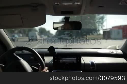 Woman driving car on parking lot near shopping mall against blur parking next to modern shopping mall at rush hour. View from vehicle&acute;s interior.