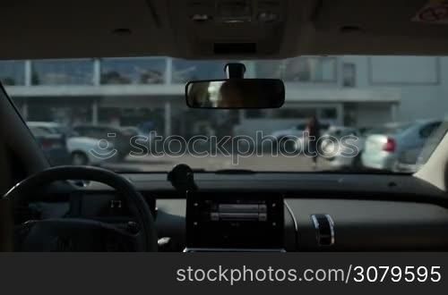 Woman driving car to exit parking lot near shopping mall with blurred trade centre on background. View from vehicle&acute;s interior. Car leaving open parking area next to trade center.