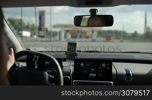 Woman driving car to refill the tank with fuel with blurred gas station on background. View from inside of vehicle. Auto running to full service petrol station to refuel.