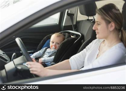 Woman driving car with baby sitting on front seat
