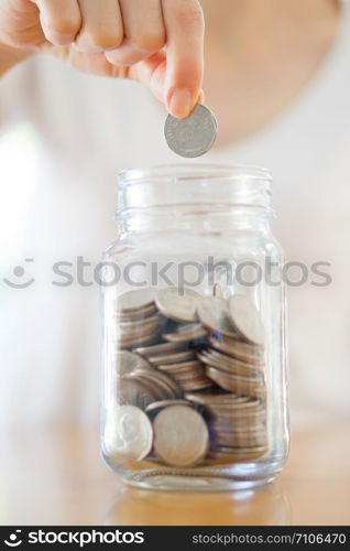 Woman Dropping Coins Into Glass Jar