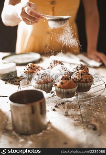 woman dusting sugar homemade muffins cooling rack