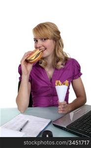 Woman eating a cheeseburger and fries at her desk