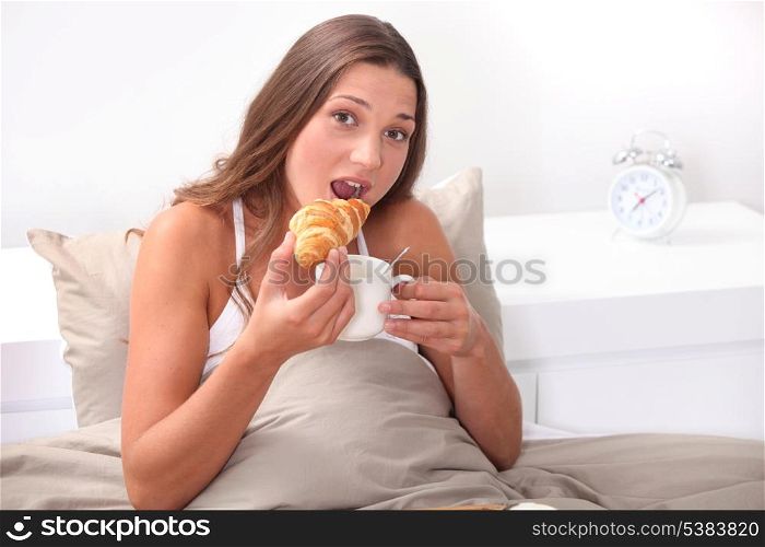 Woman eating a croissant in bed
