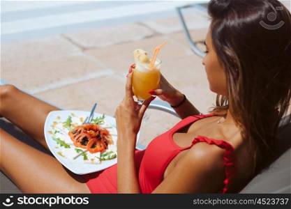 Woman eating a fresh salad and drinking juice near the pool