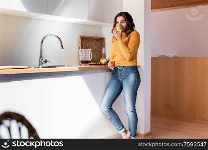 Woman eating a juicy green apple in a modern kitchen