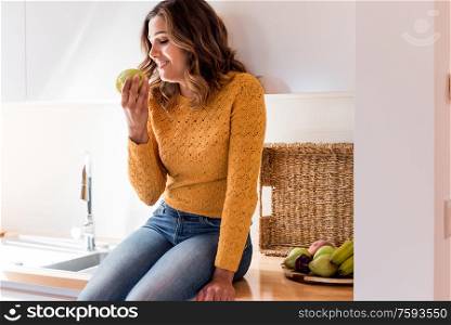 Woman eating a juicy green apple in a modern kitchen