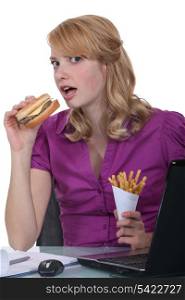 Woman eating burger and fries at desk