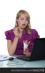Woman eating French fries at desk