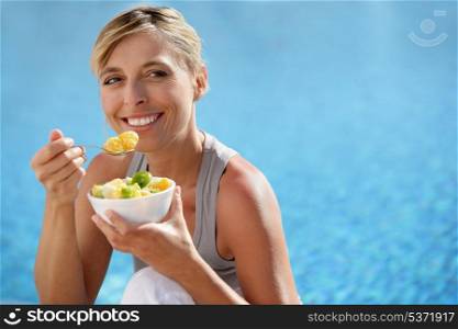 Woman eating fruit cocktail by swimming pool