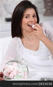 Woman eating marshmallows in bed