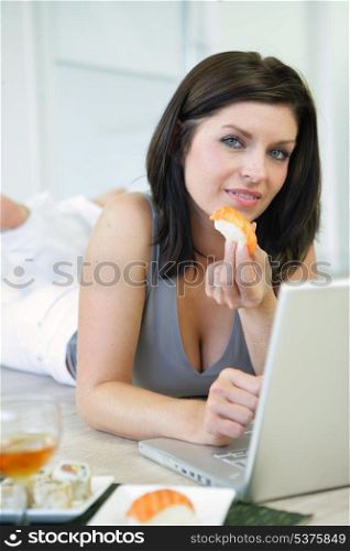Woman eating sushi working at a laptop