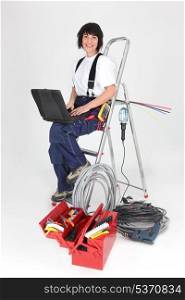 Woman electrician sitting on a ladder with laptop