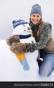 Woman embracing snowman kneeling on snow-covered hill portrait