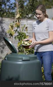 Woman Emptying Food Waste Into Garden Composter At Home