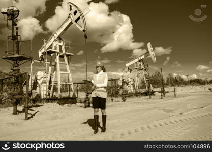 Woman engineer in glasses on the oil field wearing helmet and work clothes. Industrial site background. Oil and gas concept. Toned sepia.