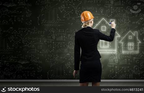 Woman engineer. Rear view of woman in hardhat drawing sketches on blackboard