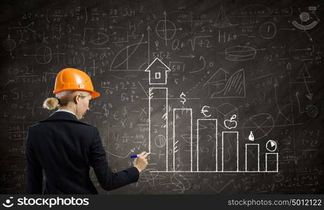 Woman engineer. Rear view of woman in hardhat drawing sketches on blackboard