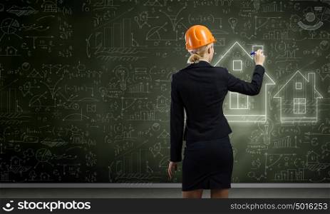 Woman engineer. Rear view of woman in hardhat drawing sketches on blackboard