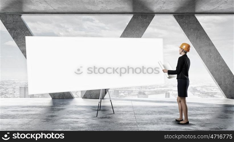 Woman engineer with banner. Attractive elegant woman in helmet in modern interior. Mixed media