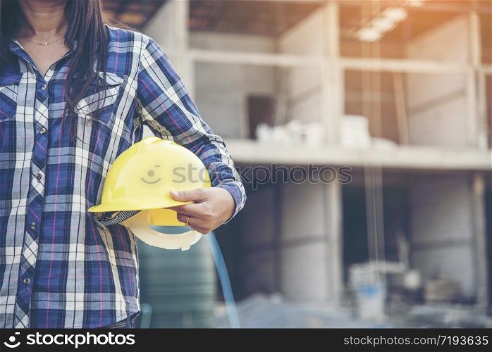 Woman engineer working on construction site and holding yellow hard hat safety helmet head protection at manufacturing industry. Construction Concept.