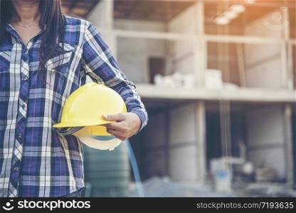Woman engineer working on construction site and holding yellow hard hat safety helmet head protection at manufacturing industry. Construction Concept.