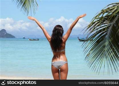 Woman enjoy tropical beach. Woman in bikini enjoying tropical beach looking at sea with raised hands