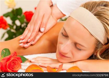 Woman enjoying a wellness back massage in a spa setting with roses in the background, she is very relaxed (close-up)