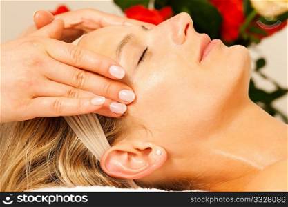 Woman enjoying a wellness head massage in a spa setting with roses in the background, she is very relaxed