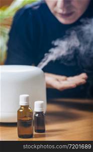 Woman Enjoying Aroma Therapy Steam Scent from Home Essential Oil Diffuser or Air Humidifier. Ultrasonic technology, increasing air humidity indoors for more comfortable living conditions. Woman Enjoying Aroma Therapy Steam Scent from Home Essential Oil Diffuser or Air Humidifier