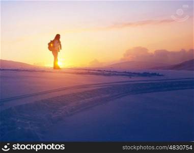 Woman enjoying beautiful sunset view from the high snowy mountain, discovering wild nature, active winter holidays