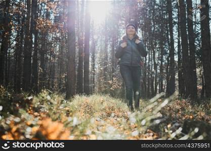 Woman enjoying hike on sunny vacation day. Female with backpack walking through forest path. Spending summer vacation close to nature