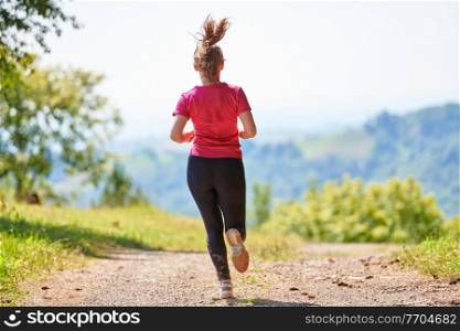 woman enjoying in a healthy lifestyle while jogging on a country road through the beautiful sunny forest, exercise and fitness concept