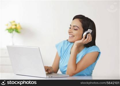 Woman enjoying music while using laptop at home