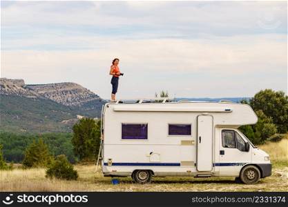 Woman enjoying trip with motor home, standing on roof of camper vehicle, holds camera, taking travel picture from mountain nature. Happiness, vacation and traveling.. Woman traveling with caravan, taking photo from rv roof