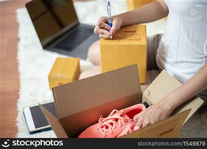 Woman entrepreneur owner SME business is checking order with smartphone, laptop and packaging box to send her customer