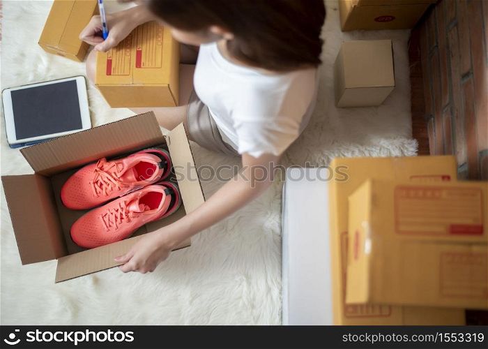 Woman entrepreneur owner SME business is checking order with smartphone, laptop and packaging box to send her customer