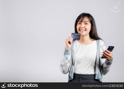 Woman excited smiling hold mobile phone and plastic debit credit bank card for payment studio shot isolated white background, happy young female using smartphone buy and pay online shopping