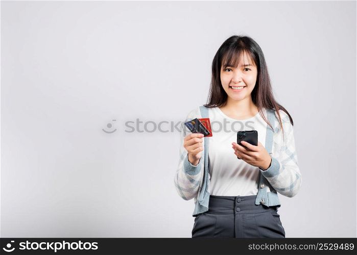 Woman excited smiling hold mobile phone and plastic debit credit bank card for payment studio shot isolated white background, happy young female using smartphone buy and pay online shopping