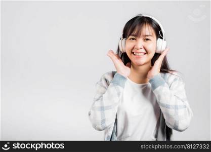 Woman excited smiling listening to music radio in bluetooth headphones and holding phone studio shot isolated white background, happy Asian young female listen modern technology mobile phone