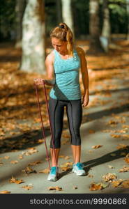 Woman Exercising Biceps With Elastic Band Outdoors in The Fall, in Public Park