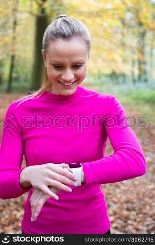 Woman Exercising In Autumn Woodland Looking At Activity Tracker On Smart Watch