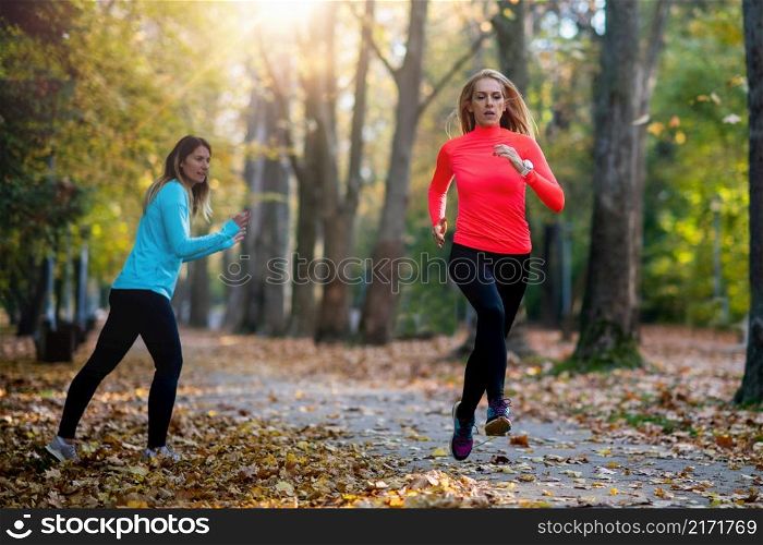 Woman Exercising in Public Park with Personal Trainer in the Fall. Trainer Cheering and Woman Running.. Woman Exercising in Public Park with Personal Trainer. Trainer Cheering and Woman Running