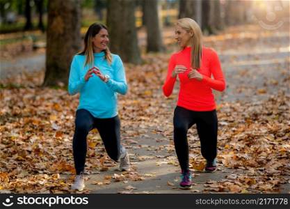 Woman Exercising in Public Park with Personal Trainer in the Fall. . Woman Exercising in Public Park with Personal Trainer. Doing Lunges Together in the Fall.