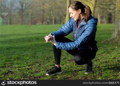 Woman Exercising In Winter Park Looking At Activity Tracker On Smart Watch