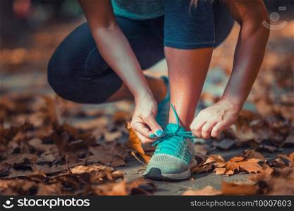 Woman Exercising Outdoors in The Fall. Kneeling and tying shoe.
