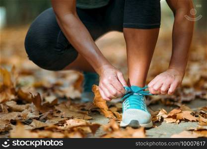 Woman Exercising Outdoors in The Fall. Kneeling and tying shoe.