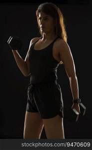 Woman exercising with dumbbells in front of a dark background.